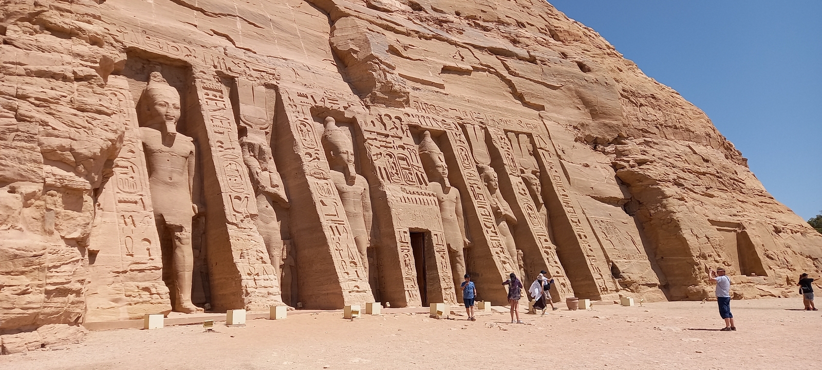 Groupe de personnes explorant la grande façade d'un temple égyptien avec des statues colossales.