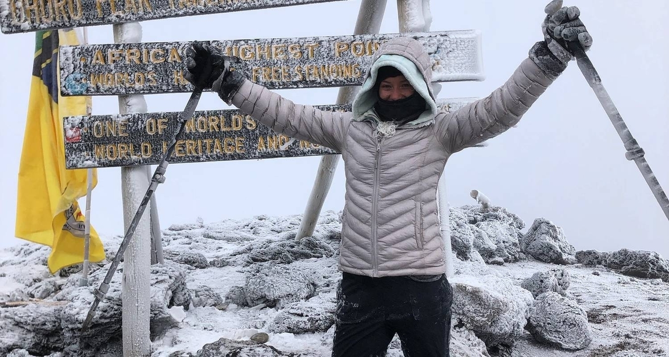 Personne célébrant au sommet enneigé d'Uhuru Peak avec des panneaux indicateurs.