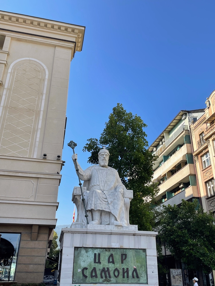 Statue d'une figure assise avec une croix dans une ville animée.