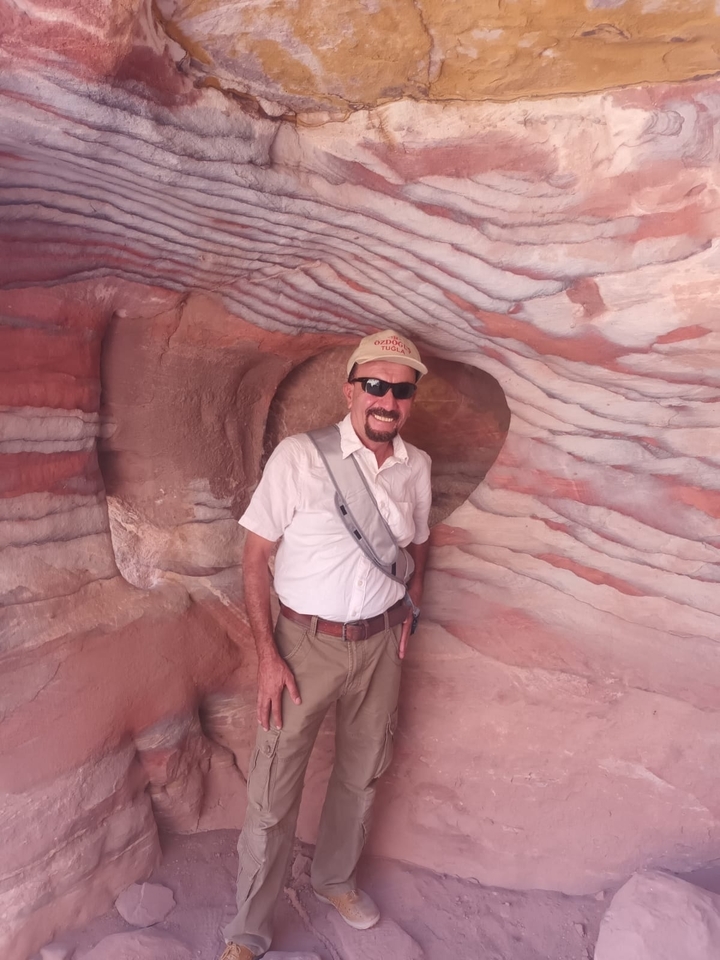 Homme posant devant une grotte de grès colorée.
