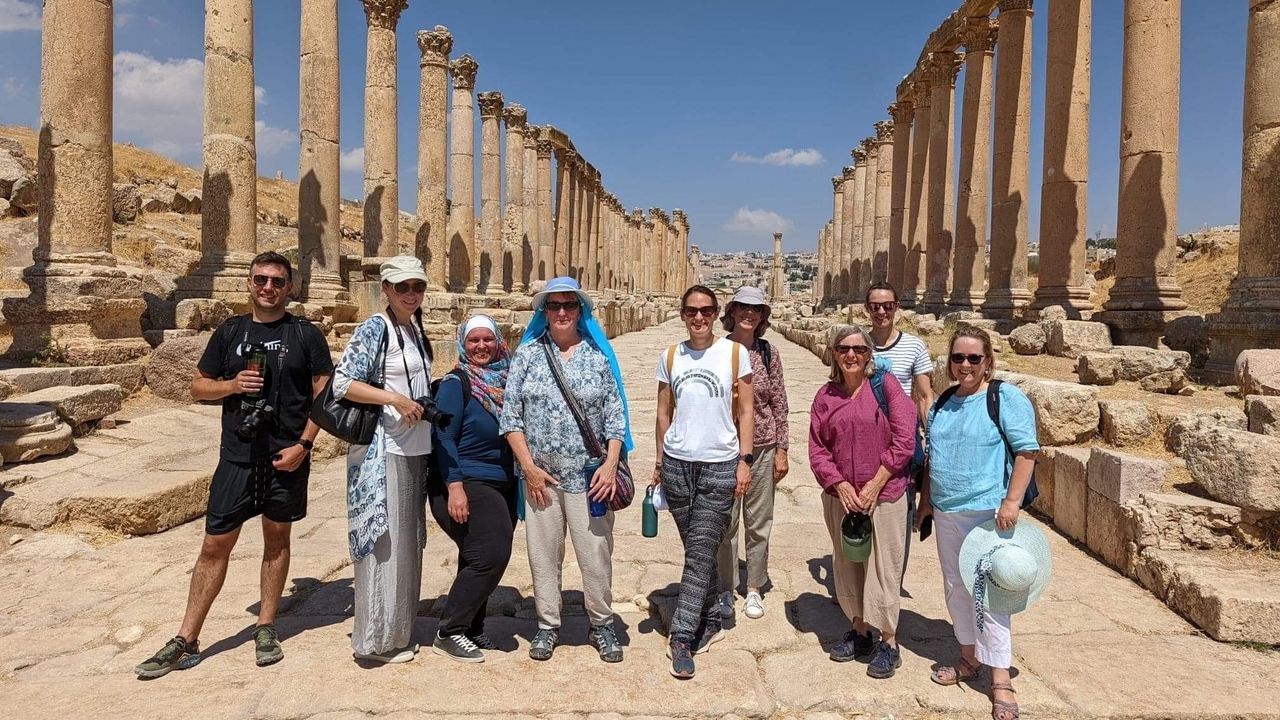 Un groupe de touristes souriant devant des ruines antiques avec des colonnes.