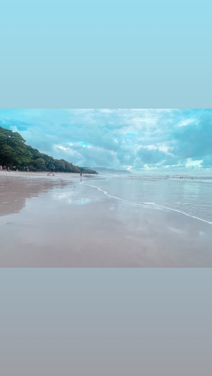Plage tranquille avec reflet sur le sable mouillé et collines lointaines.