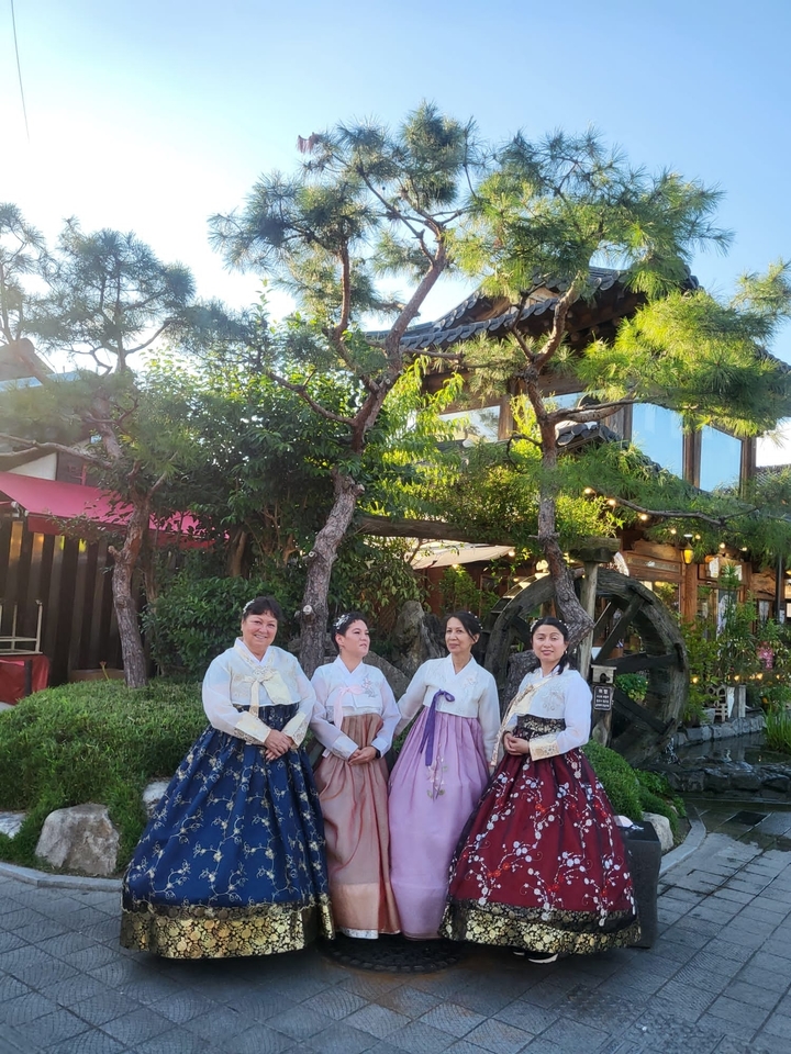 Des femmes vêtues de Hanbok traditionnel posent devant un jardin.