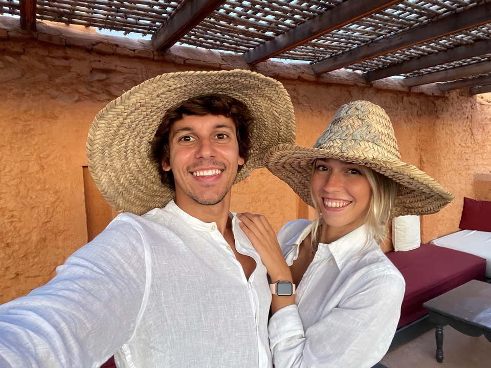 Deux personnes souriantes avec de grands chapeaux de paille et un mur texturé derrière