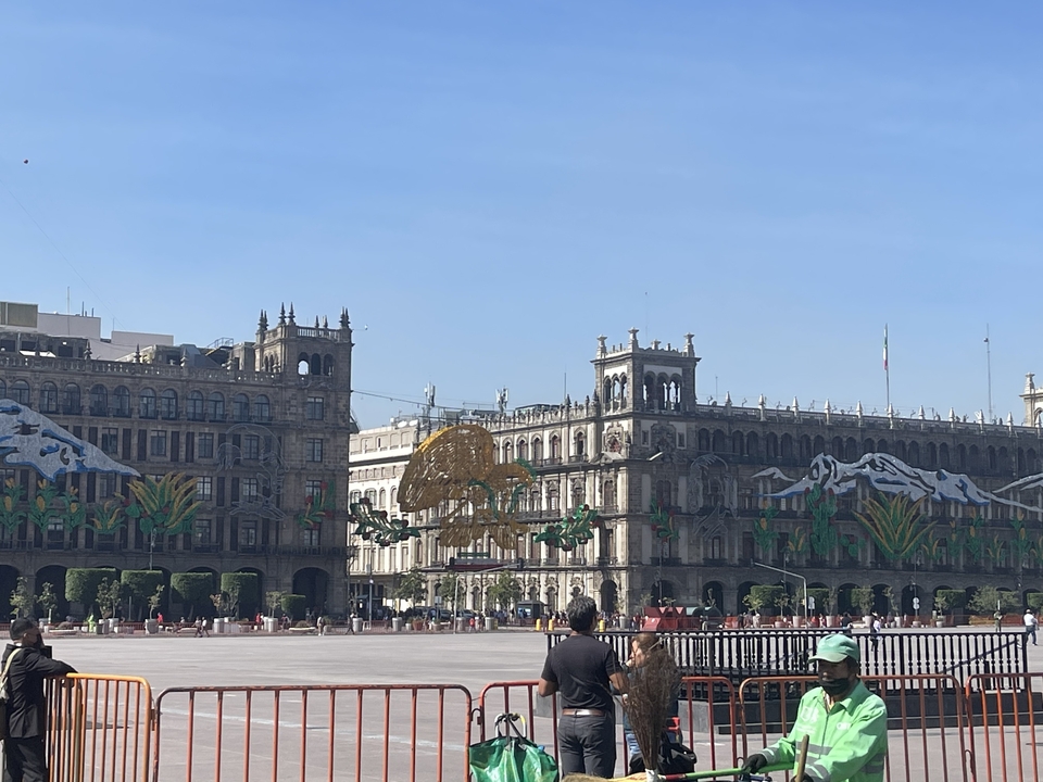 Grande place historique avec des gens et de grands bâtiments anciens décorés de drapeaux et symboles mexicains.