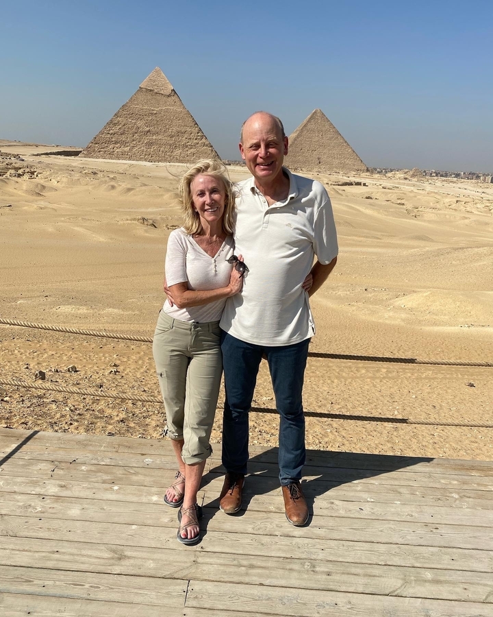 Couple posant dans un paysage désertique avec des ruines archéologiques en arrière-plan.