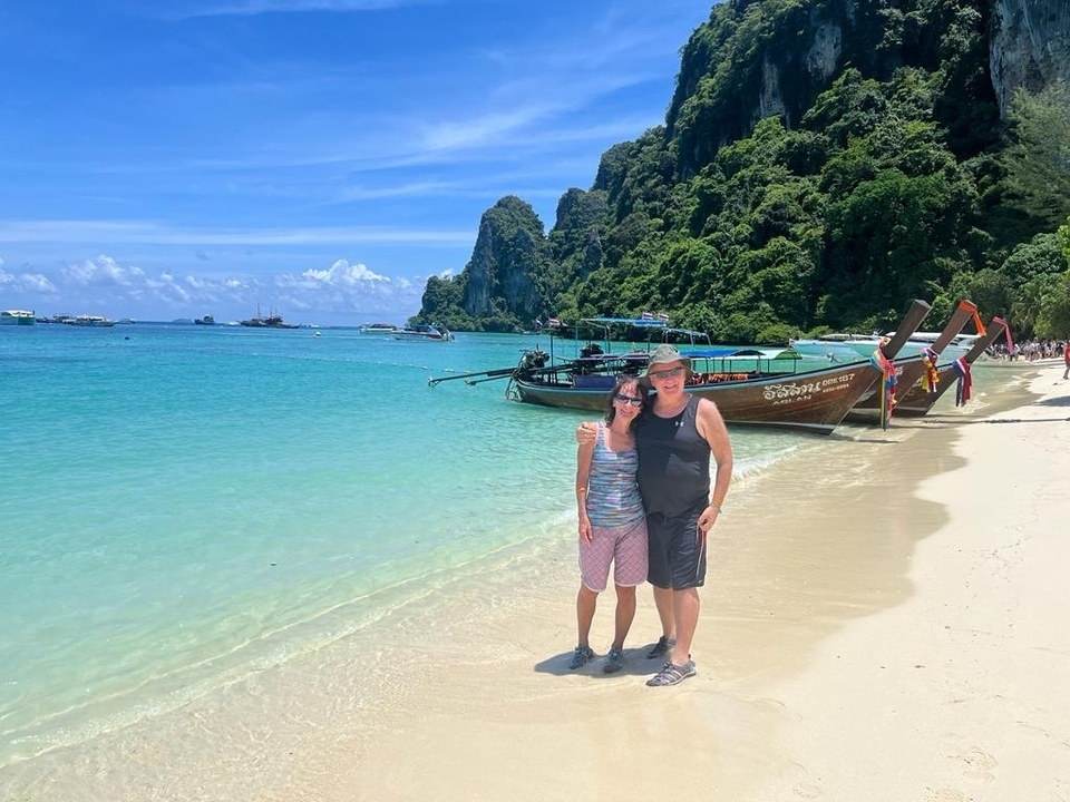 Couple posant sur une magnifique plage avec des eaux turquoise et des bateaux.