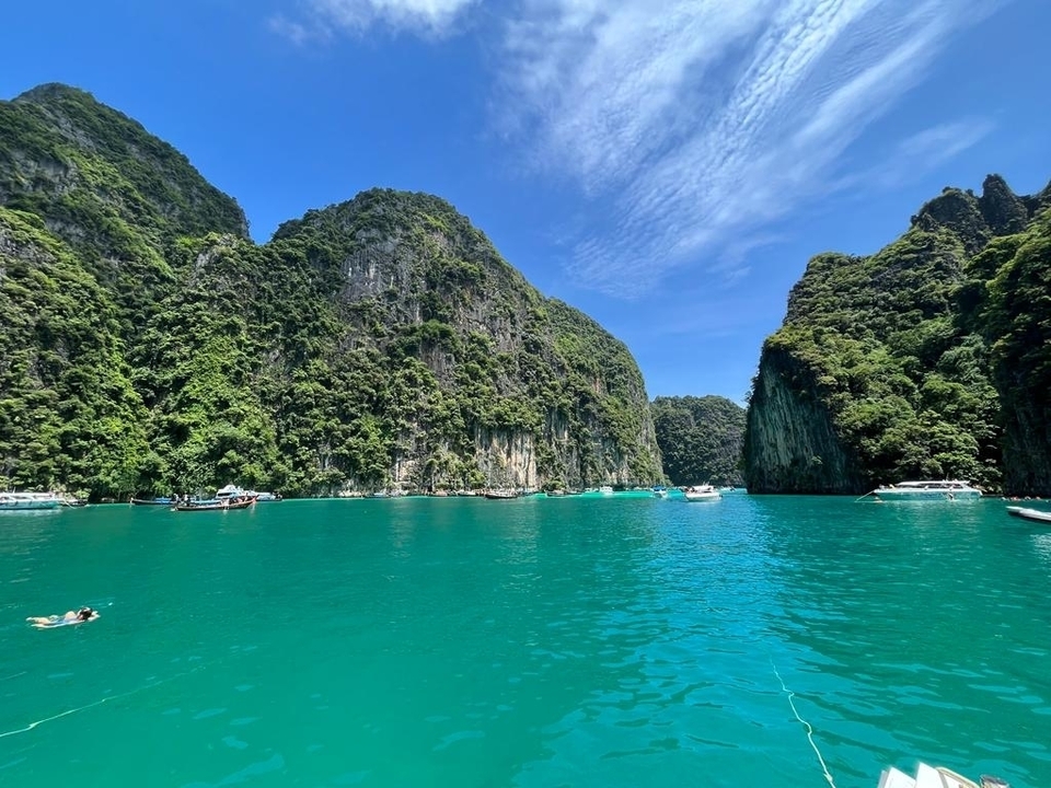 Vue panoramique d'une baie turquoise entourée de falaises luxuriantes avec des gens qui nagent.