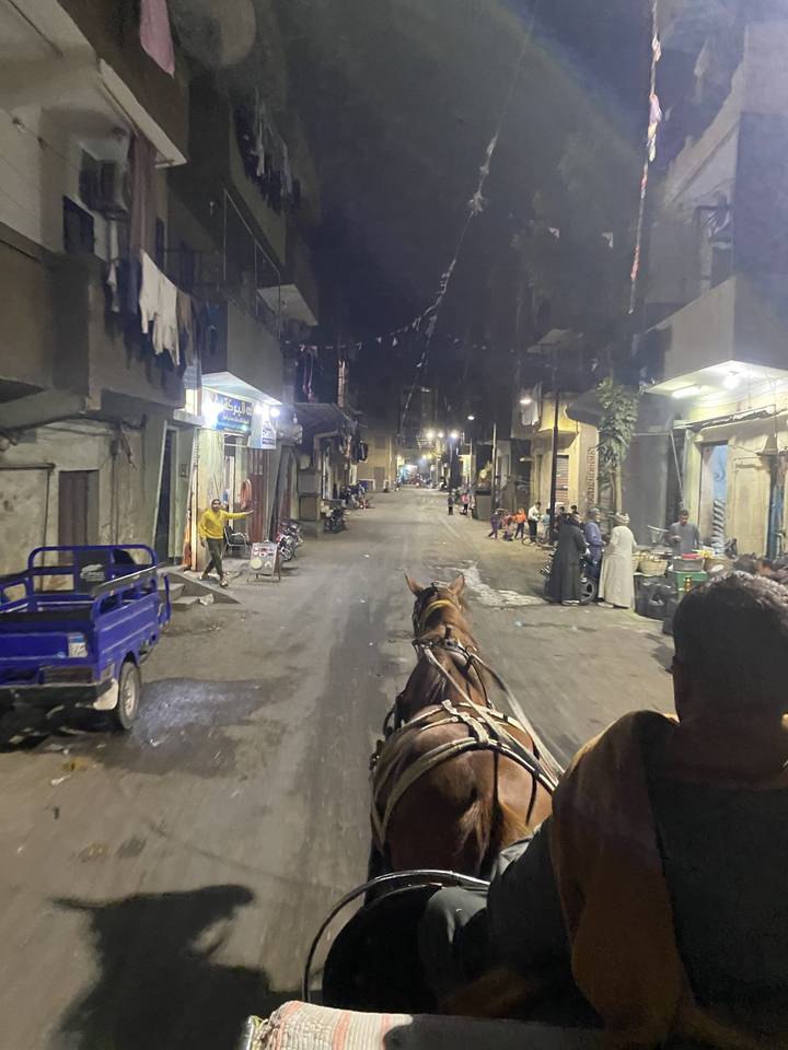 People riding in a horse-drawn carriage through a street at night.