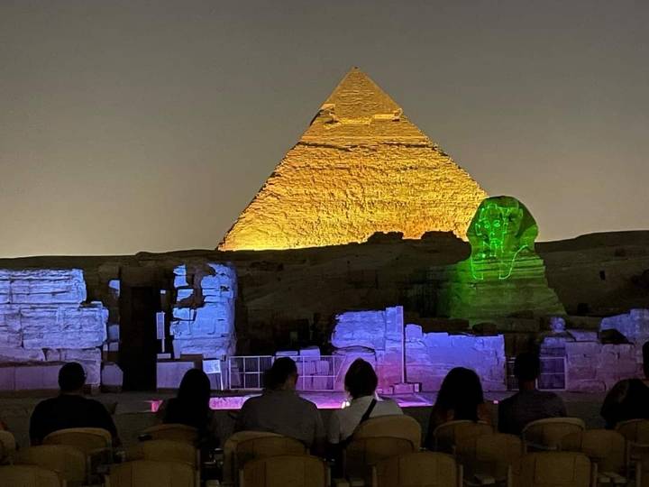 Pyramides et Sphinx illuminés par des lumières colorées la nuit.