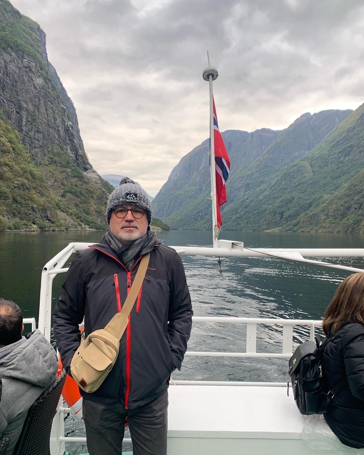 Personne sur un bateau avec un drapeau norvégien et des fjords en arrière-plan.