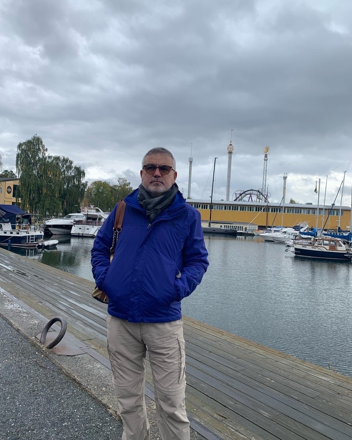 Homme debout près d'un port de plaisance avec des bateaux en arrière-plan.