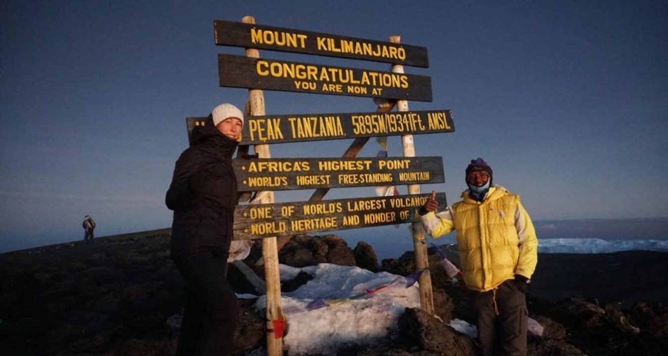 Des personnes posant à côté d'un panneau du sommet du mont Kilimandjaro.