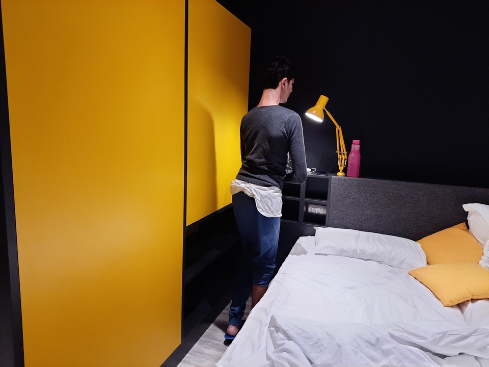 Personne dans une chambre avec un lit et une décoration jaune.