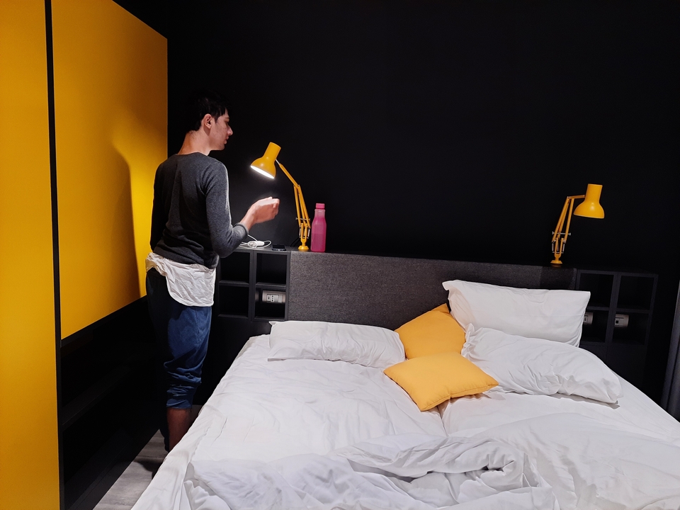 Personne debout à côté d'un lit avec des accents jaune vif.