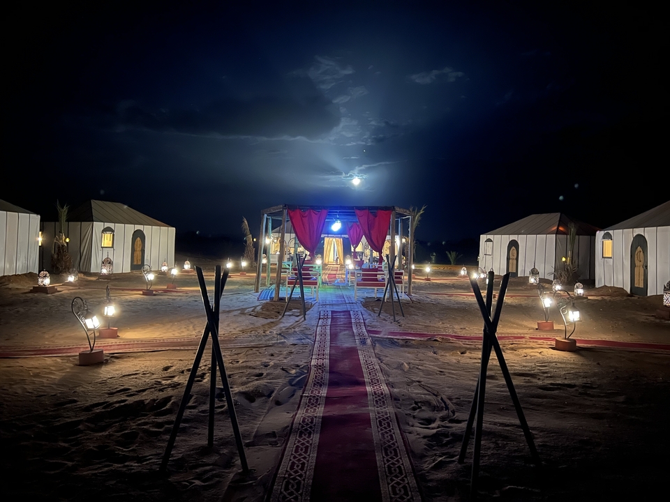 Camp du désert bien éclairé avec des tentes et des lanternes la nuit.
