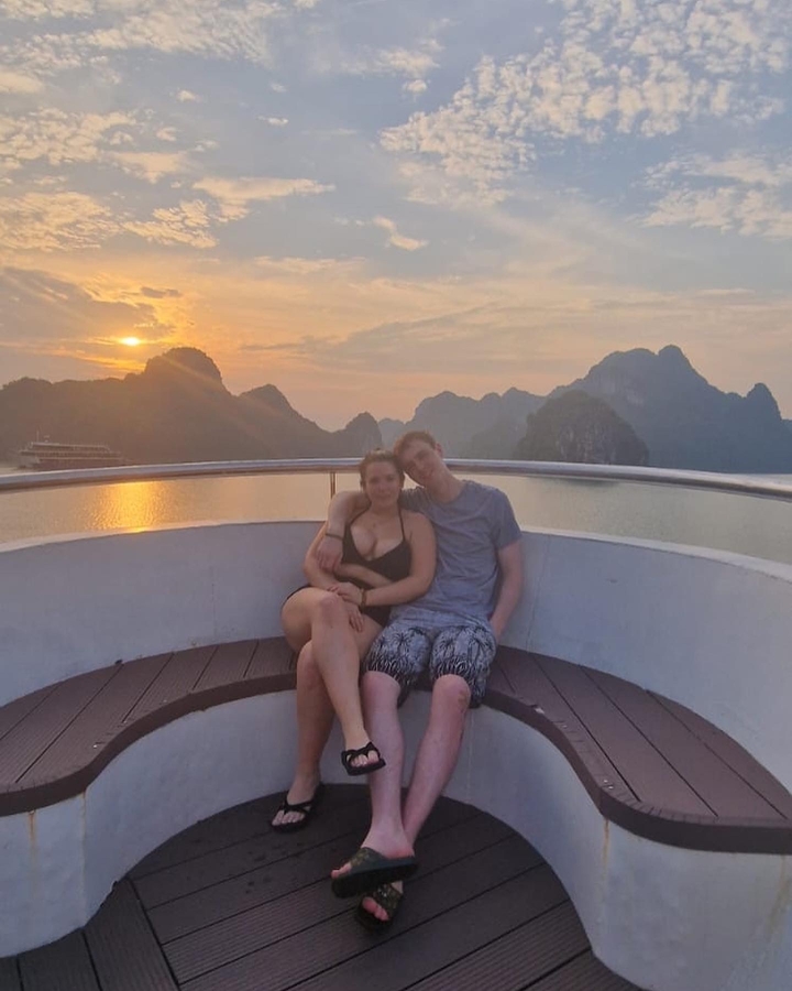 Couple assis sur un bateau au coucher du soleil avec de majestueuses falaises calcaires en arrière-plan.