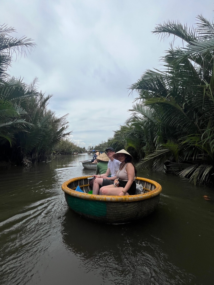 Des gens naviguent dans un bateau-panier circulaire en bambou sur une rivière bordée de verdure luxuriante.