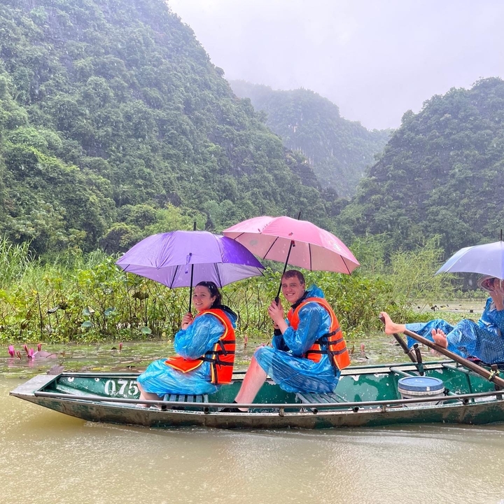 Des gens avec des parapluies dans un bateau entouré de montagnes verdoyantes.