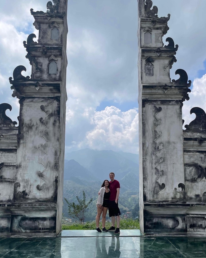 Couple debout entre deux hautes colonnes richement sculptées avec des montagnes en arrière-plan.