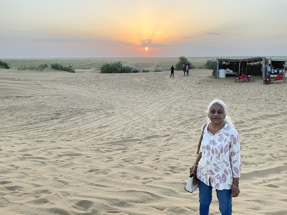 Femme debout sur une dune de sable avec un coucher de soleil en arrière-plan.