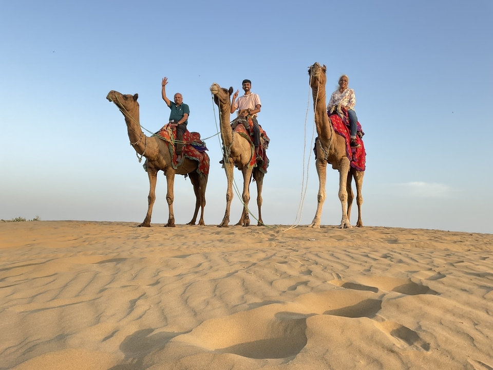 Trois personnes sur des chameaux se tenant debout sur des dunes de sable sous un ciel clair.