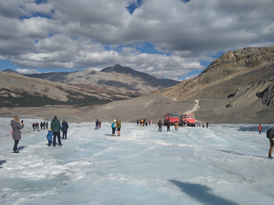 Des touristes marchant sur un glacier avec des montagnes en arrière-plan.