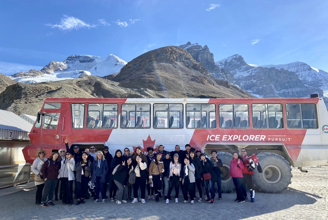 Groupe à côté d'un véhicule « Explorateur des glaces » avec des montagnes enneigées.