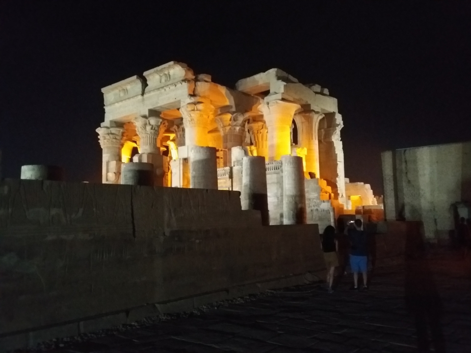 Temple ancien illuminé la nuit avec des touristes à proximité.