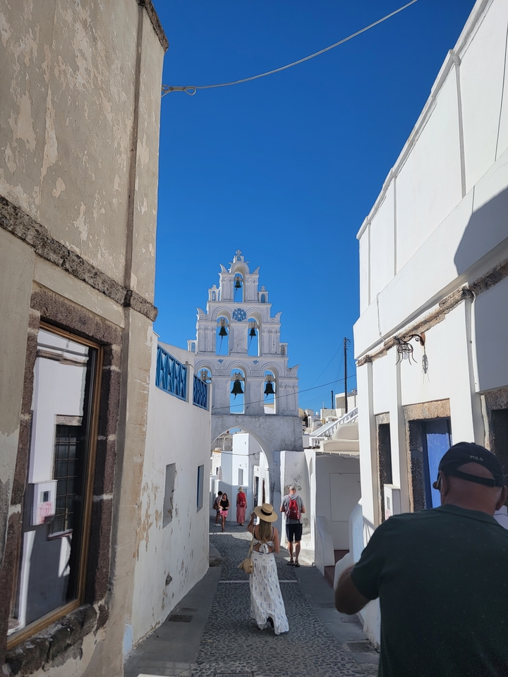 Tour de cloches avec une façade blanche et en pierre dans une ruelle étroite.