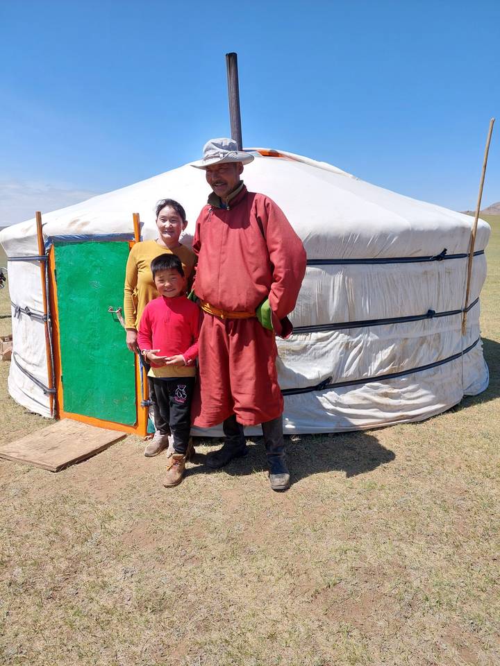 Famille posant devant leur yourte en tenue traditionnelle.