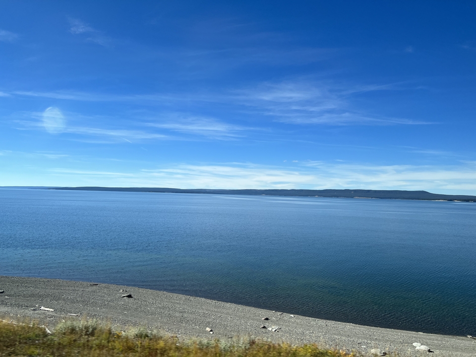 Vaste lac avec un ciel bleu clair et des collines au loin.