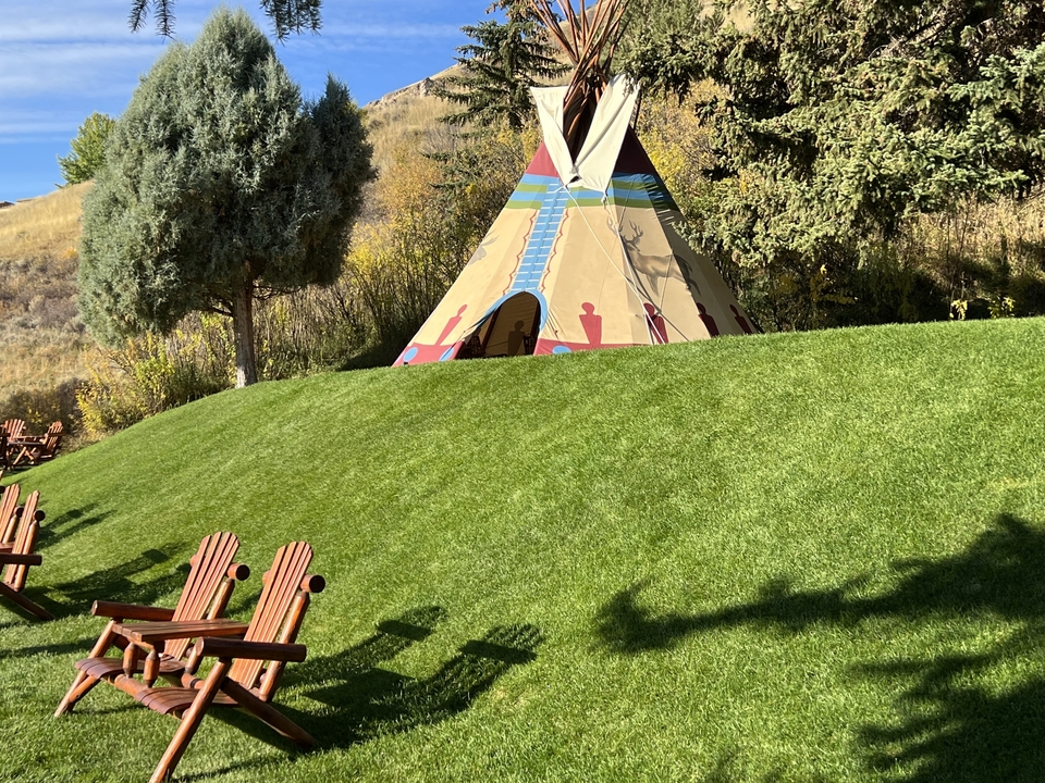 Tipi coloré et chaises en bois sur une colline herbeuse.