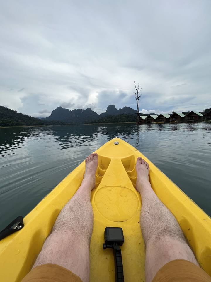Feet visible on a yellow kayak on a lake with mountains.