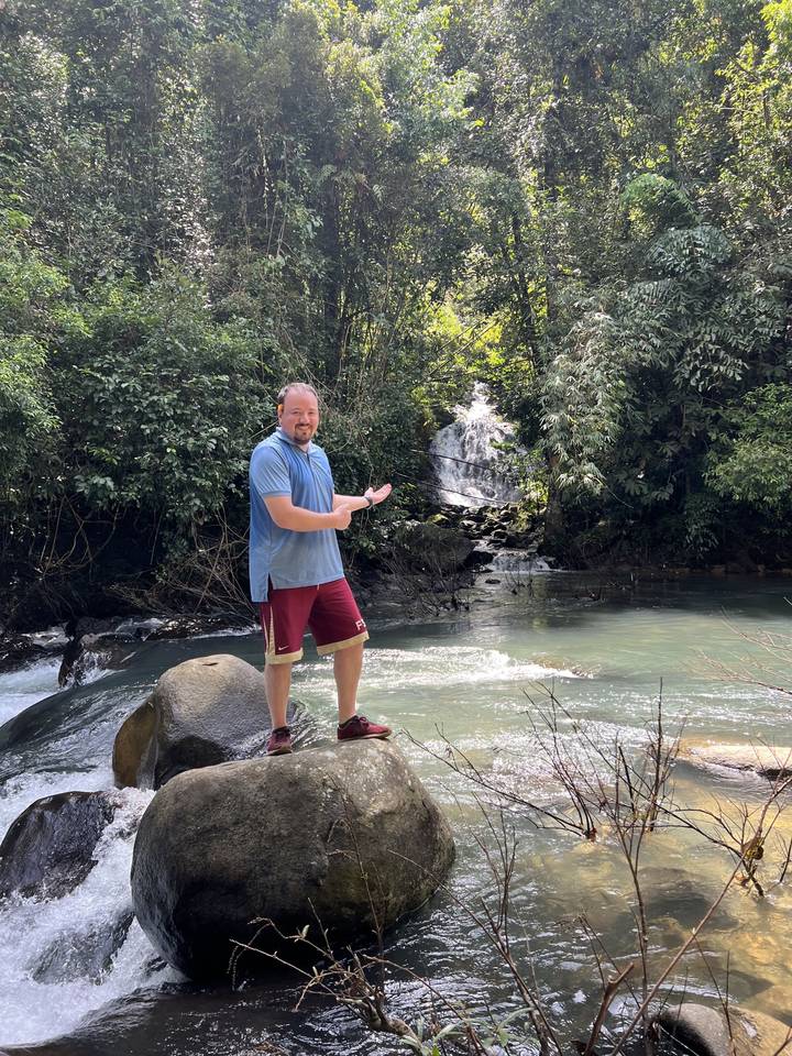 Individual standing on rocks by a waterfall.
