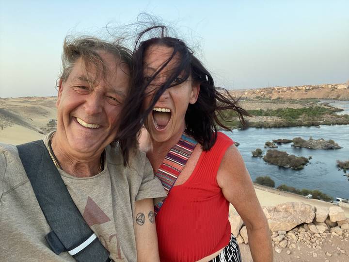 Ein Paar lächelt mit einem Fluss und einer Wüstenlandschaft im Hintergrund.