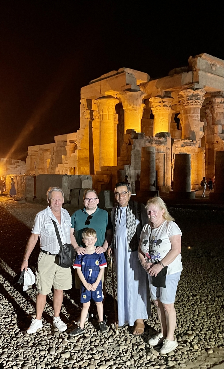 Groupe de personnes devant des ruines antiques illuminées la nuit.