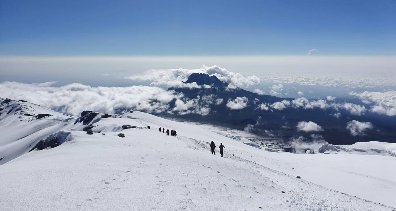 Randonneurs sur un paysage montagneux enneigé avec une vue sur les nuages en contrebas.