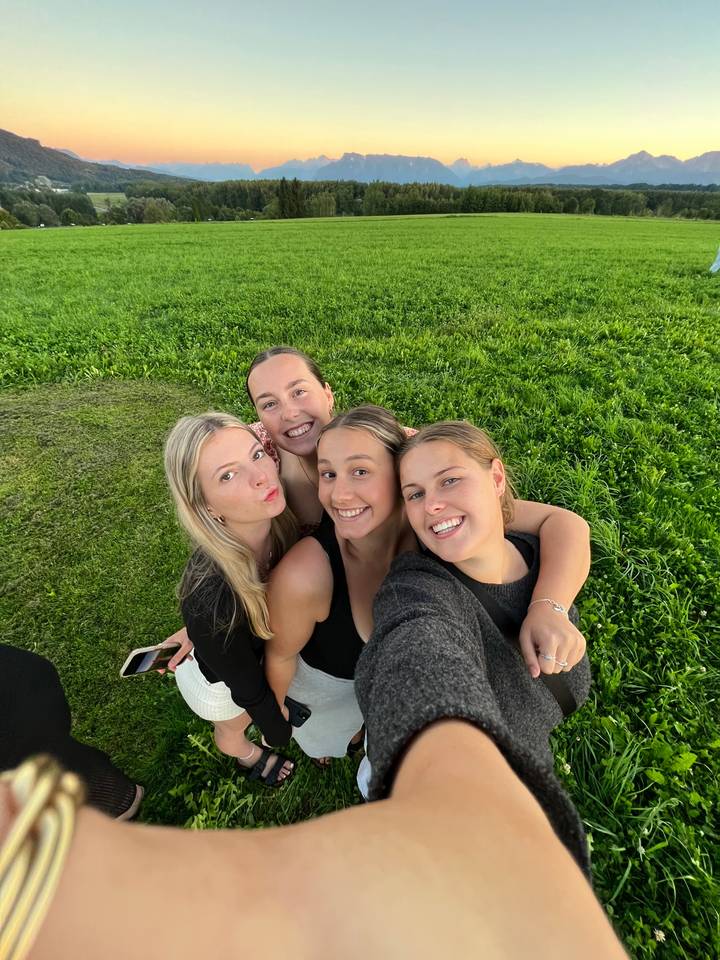 Un selfie de petit groupe dans un champ herbeux avec un paysage de montagne en arrière-plan.