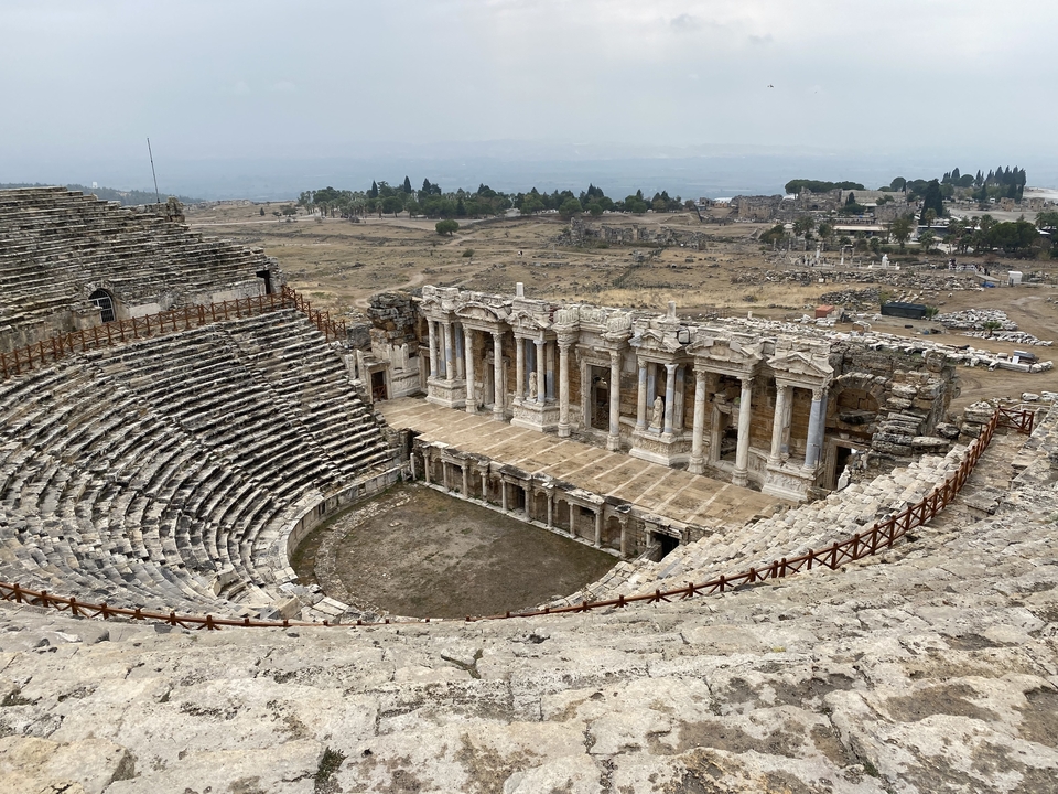 Une ruine d'amphithéâtre antique avec des gradins en pierre et une grande scène dans un paysage aride.