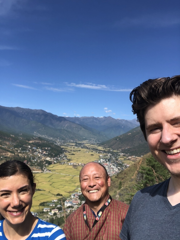Une personne souriante avec des collines et un paysage urbain en arrière-plan.