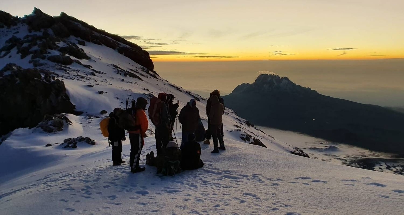 Groupe d'alpinistes sur une montagne enneigée au lever du soleil.