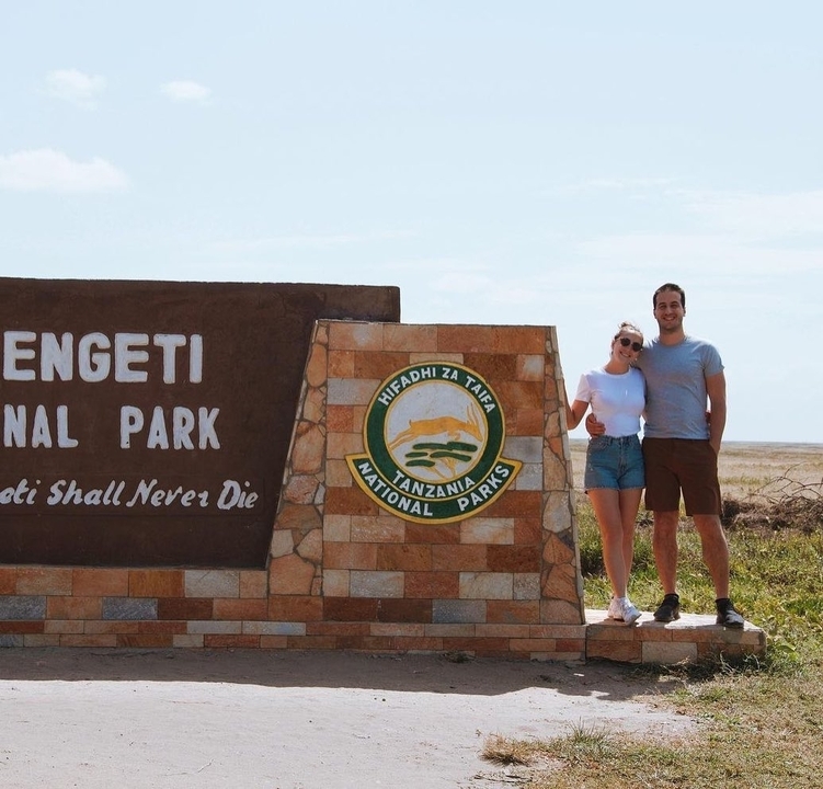 Couple debout à côté d'un panneau du parc national du Serengeti.