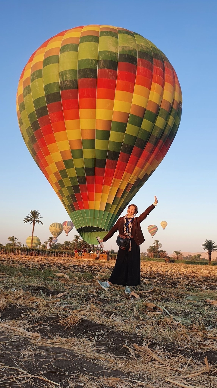 Femme posant joyeusement à côté de montgolfières colorées.