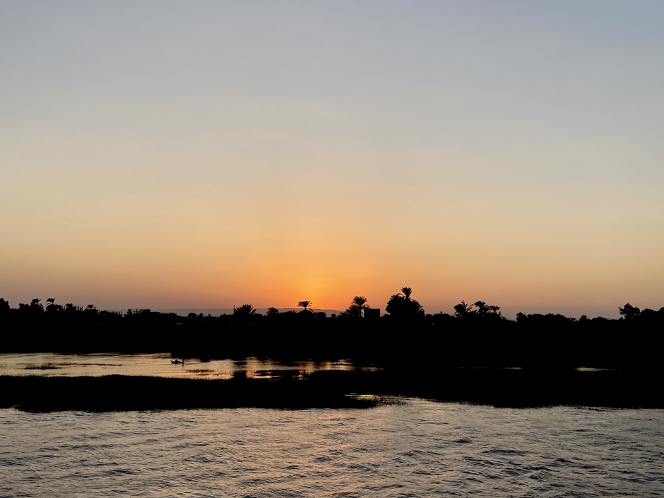 Vue du coucher de soleil sur une rivière avec des arbres en silhouette.