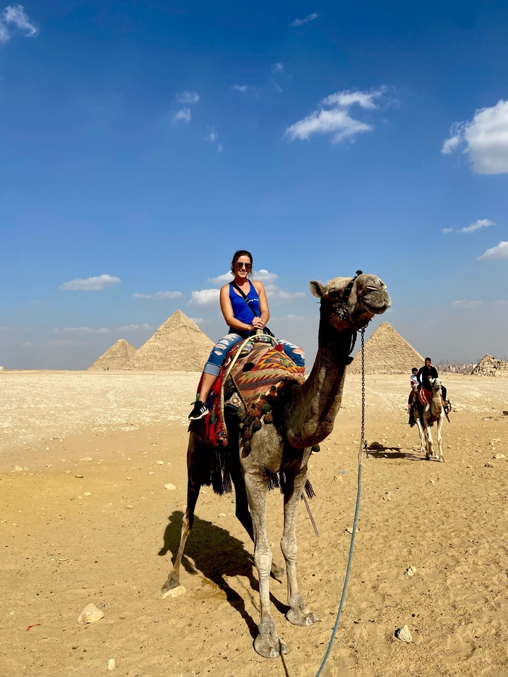 Personne montant un chameau avec les pyramides de Gizeh en arrière-plan.