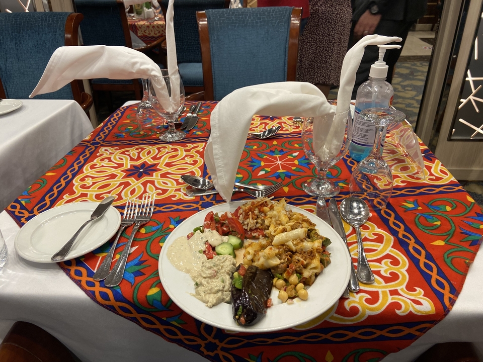 Table dressée avec une assiette de nourriture, des couverts et des verres sur une nappe à motifs.