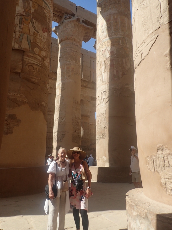 Deux femmes avec des chapeaux se tenant debout parmi de grandes colonnes antiques.