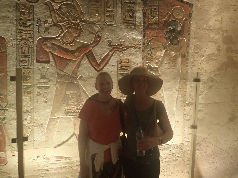 Deux femmes posant devant des sculptures murales de l'Égypte antique.