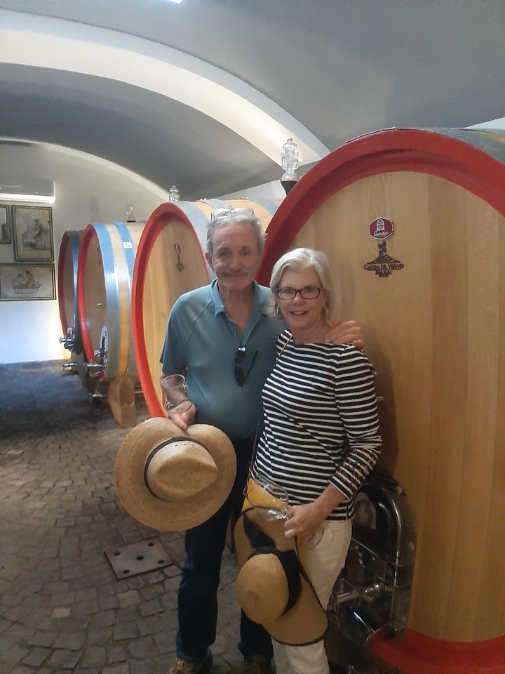 Couple posant devant de grands tonneaux de vin dans une cave viticole.